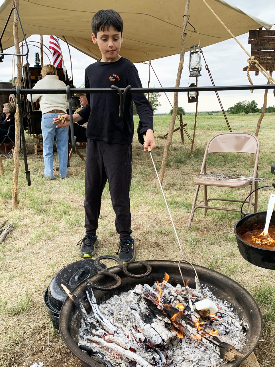S’MORE IN PROGRESS in his right hand, Conner Baskerville roasts a marshmallow to add to his graham cracker and chocolate. The occasion was a cookout at Doans, Texas on Saturday, May 1, the evening before the 143rd Doan’s May Picnic. In the background is Jeff Bearden’s authentic chuck wagon and a U. S. Flag with 36 stars, true to the era of the trail drives that crossed at nearby Doan’s Crossing. Historic Doans is 16 miles north of Vernon. | HANABA MUNN WELCH