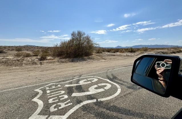 THEROADTOAMBOY beckons with the Route 66 shield painted on the pavement and the mountain range across the desert in the distance.