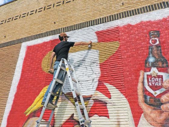 BOB WILLS WALL Leaving Bob Wills’ familiar visage till last, muralist Matt Tomlinson works atop a ladder last week in Turkey, spraying some paint to delineate the edge of Wills’ traditional Western hat. A plaster surface would have made the job easier, but brick walls are less likely to deteriorate. | HANABA MUNN WELCH