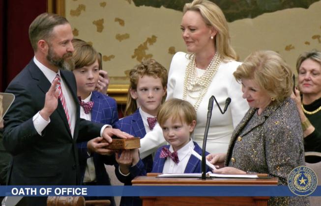 ELECTED TX SPEAKER State Rep. Dustin Burrows was administered the oath of office as Speaker of the Texas House by Secretary of State Jane Nelson (right) during opening day ceremonies on the House floor on Tuesday, Jan. 14, 2025, as Burrows’wife, Elisabeth (in white dress), and children look on. | BOB DAEMMRICH FOR THE TEXAS TRIBUNE