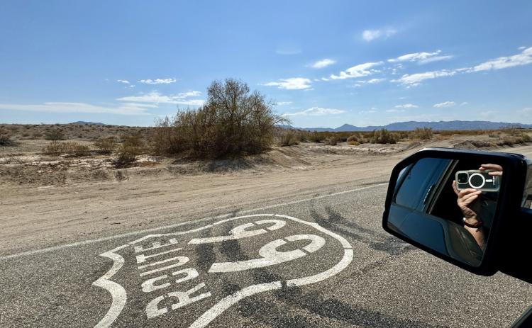 THEROADTOAMBOY beckons with the Route 66 shield painted on the pavement and the mountain range across the desert in the distance.