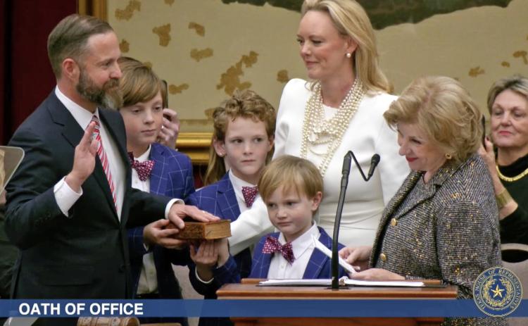ELECTED TX SPEAKER State Rep. Dustin Burrows was administered the oath of office as Speaker of the Texas House by Secretary of State Jane Nelson (right) during opening day ceremonies on the House floor on Tuesday, Jan. 14, 2025, as Burrows’wife, Elisabeth (in white dress), and children look on. | BOB DAEMMRICH FOR THE TEXAS TRIBUNE